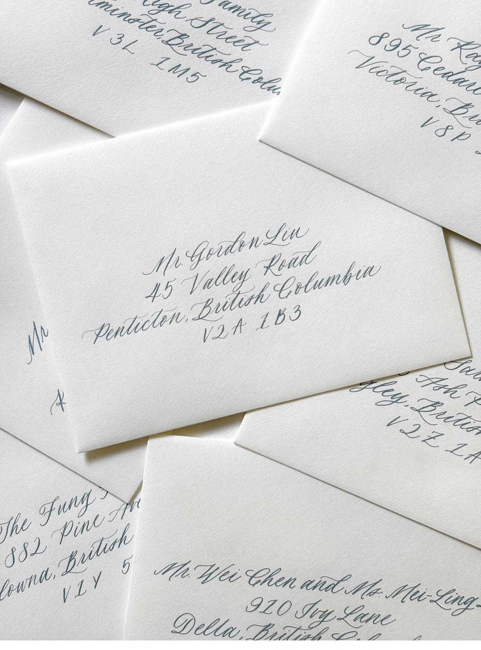 A stack of white envelopes hand-addressed in blue-grey calligraphy ink